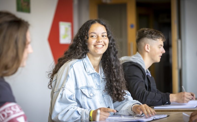 Female student sitting at desk, smiling into camera.