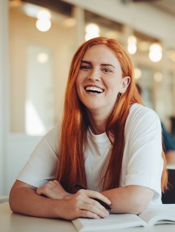 A woman laughing, seated in a bright room with string lights in the background.