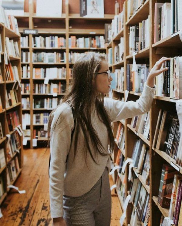 A woman browsing books on tall shelves in a library.