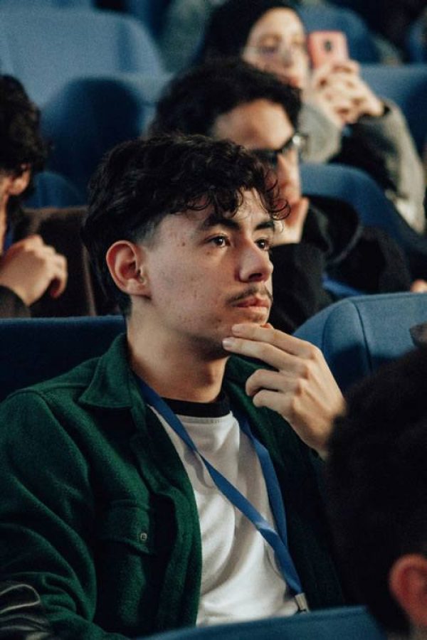 A young man sitting in a lecture theatre or cinema, resting his chin on his hand, looking thoughtful.