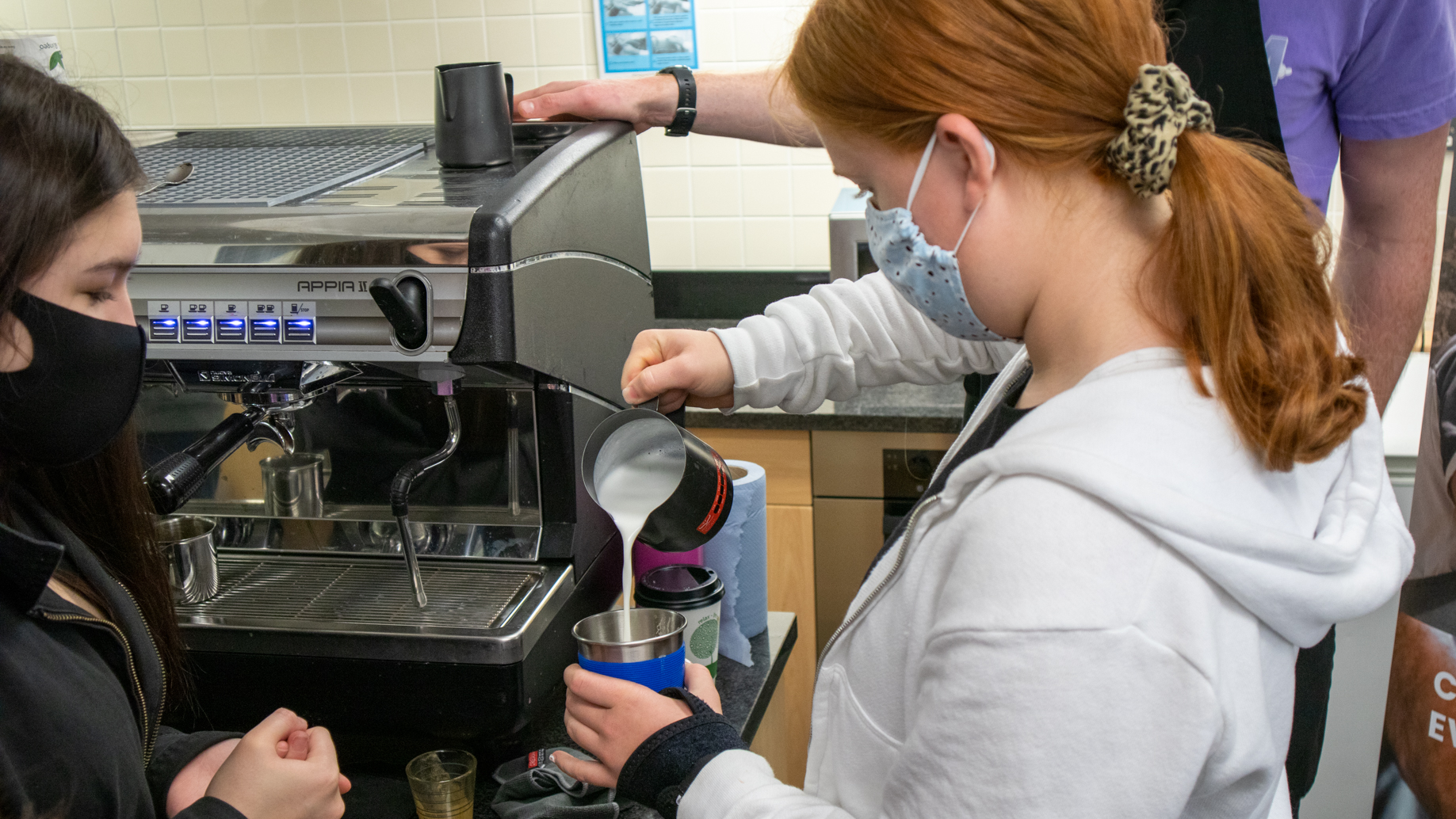 Student pouring milk into a coffee