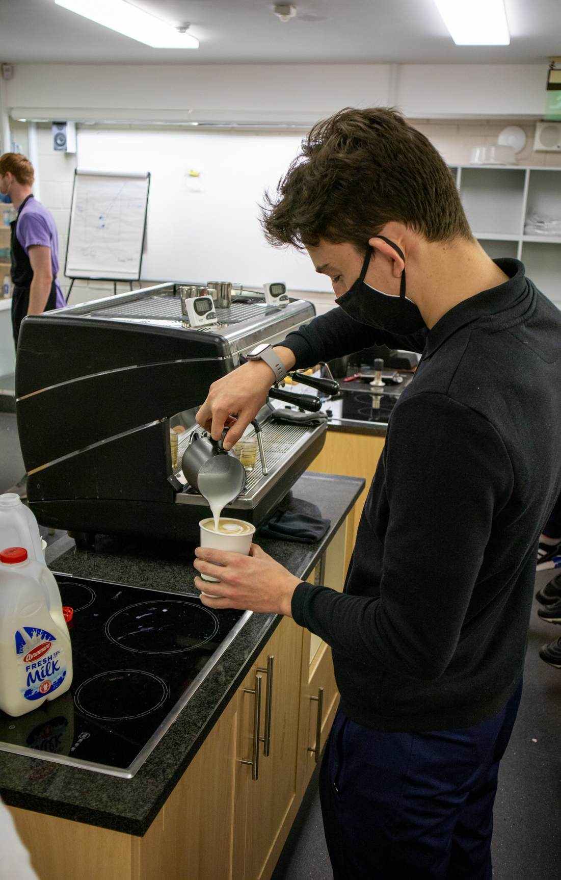 Student pouring milk into a coffee