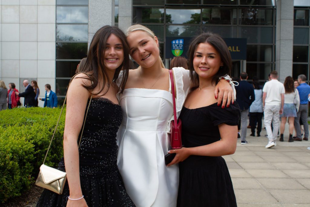 Three students in formal dresses smiling together, celebrating graduation