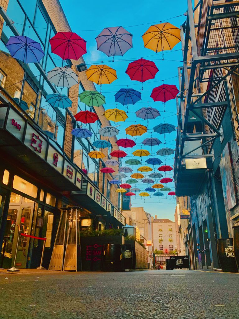 Photograph of a commercial street, with a series of colourful umbrella tops stringed between buildings