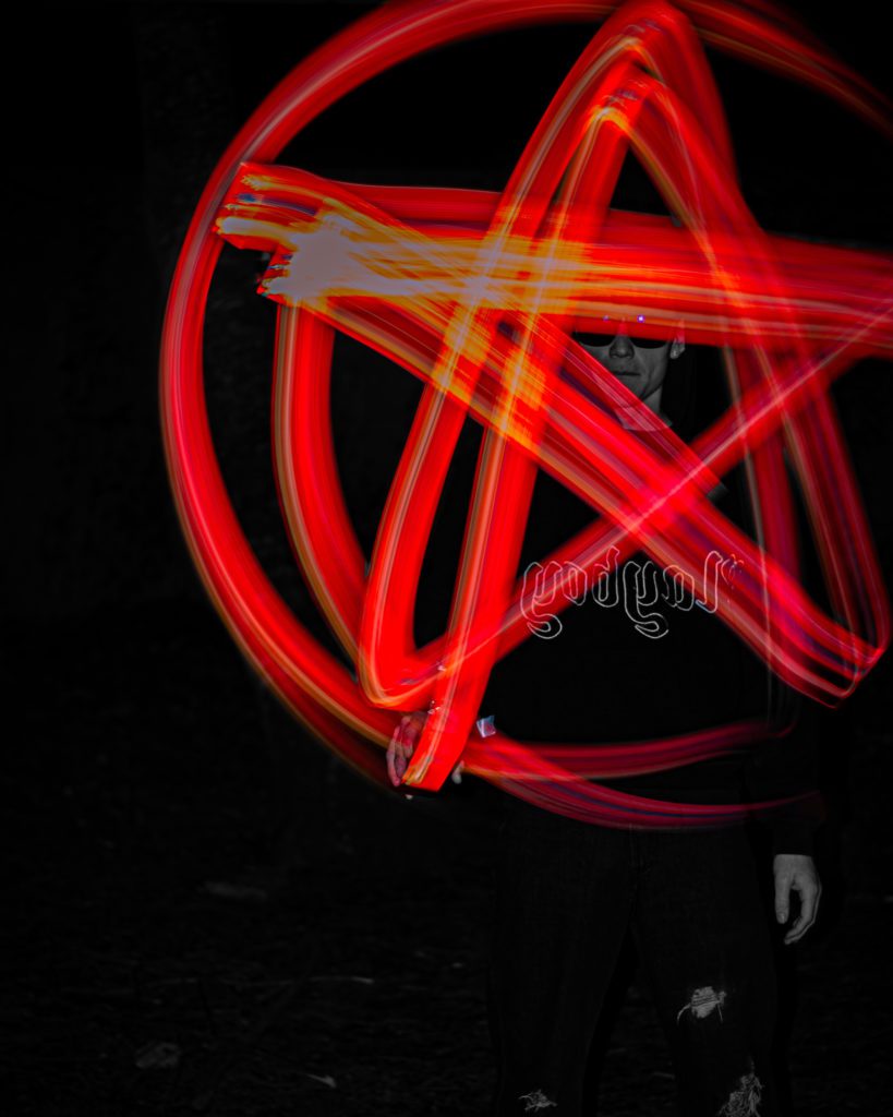 Blurred Red glowing pentagram, over a man wearing sunglasses with a black background.