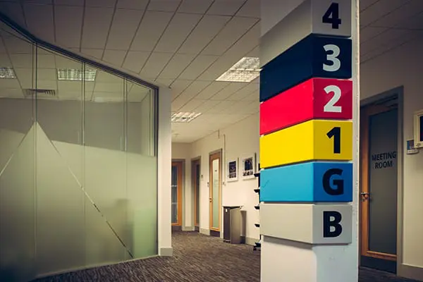 A corridor with a large floor-directory column showing levels 4, 3, 2, 1, G and B in different colours, next to a meeting room door.
