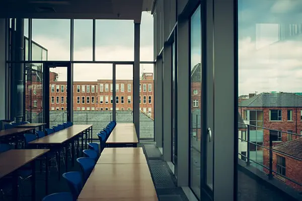 A glass-walled study area with rows of wooden tables and blue chairs, overlooking Dublin rooftops through floor-to-ceiling windows.

