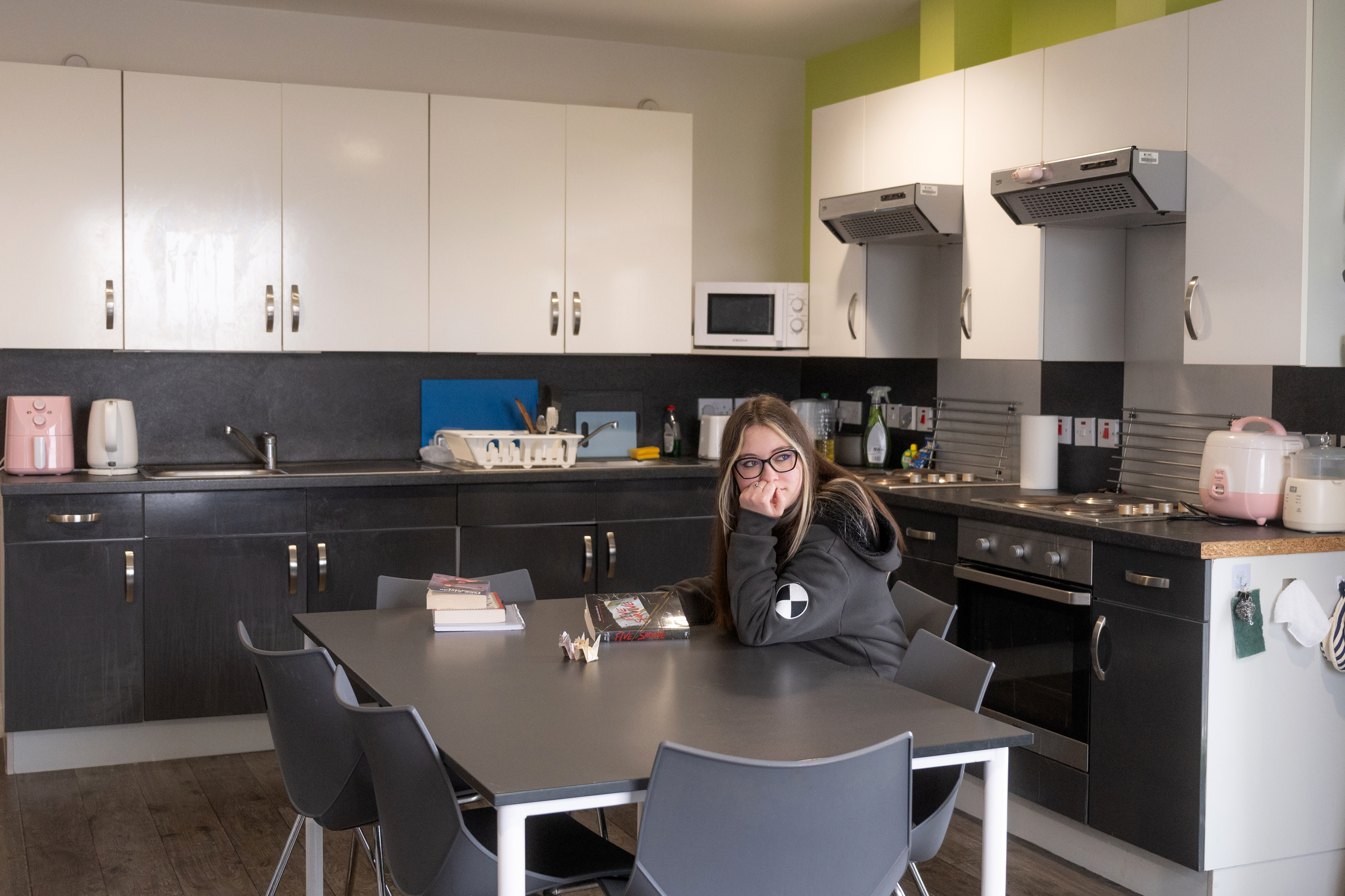 Kitchen: Shared kitchen with dark cabinetry, table and stools, students cooking or seated at the table.