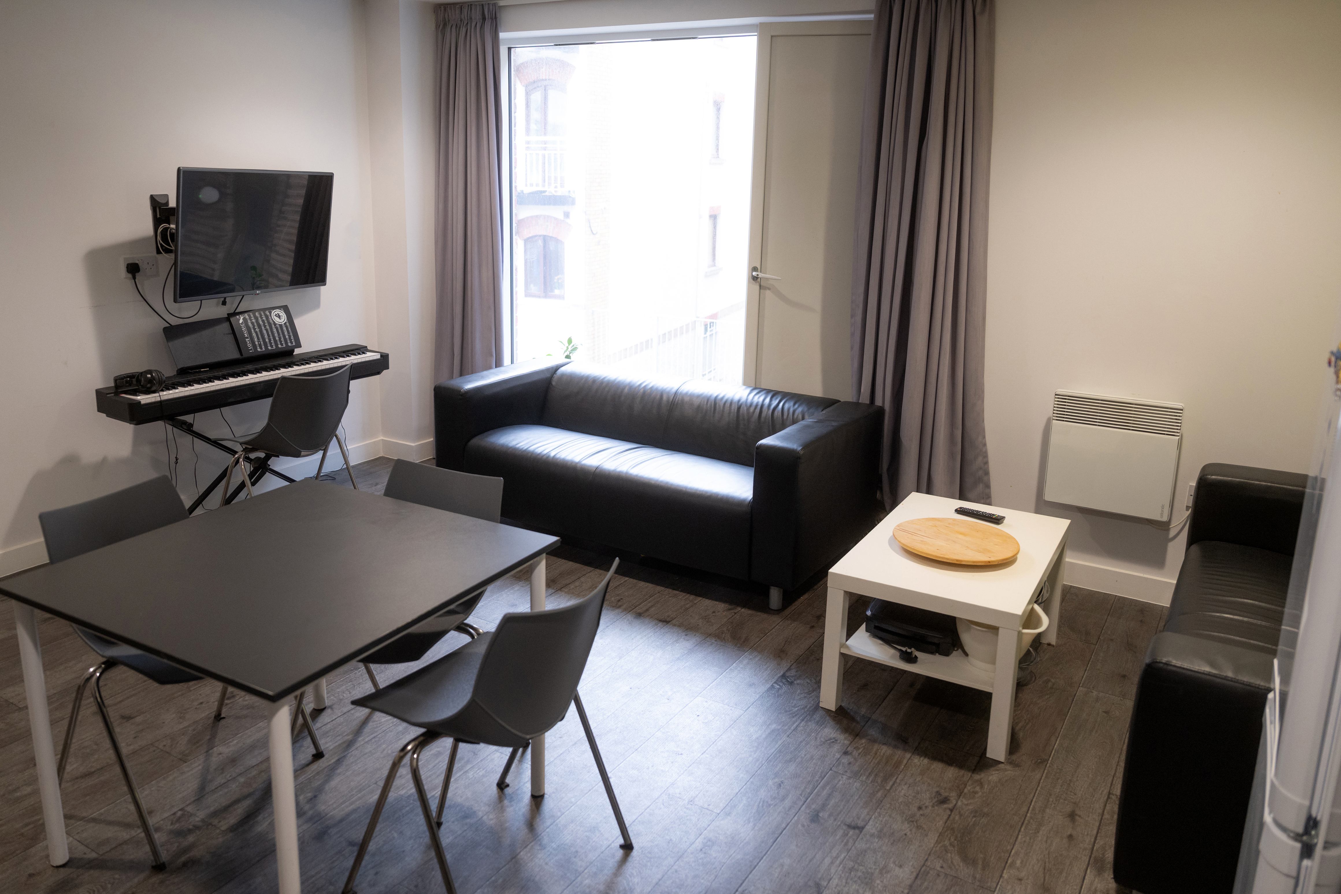 Common room with sofas: Lounge area with black sofas, coffee table, TV screen and two students relaxing.