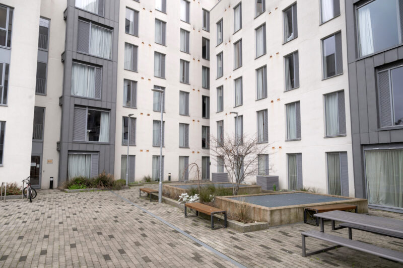 Courtyard at Binary Hub student accommodation, surrounded by a modern multi-storey building with large windows, planters and outdoor seating.