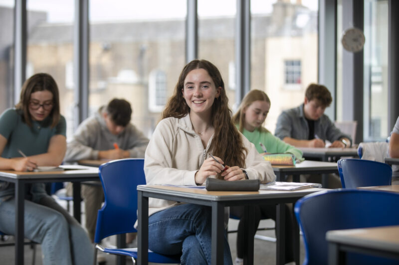 Student sitting at desk, smiling into the camera