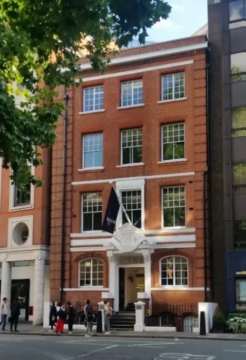 Front view of the Dukes Education building, a red-brick Georgian building with white pillared entrance and students gathered outside.