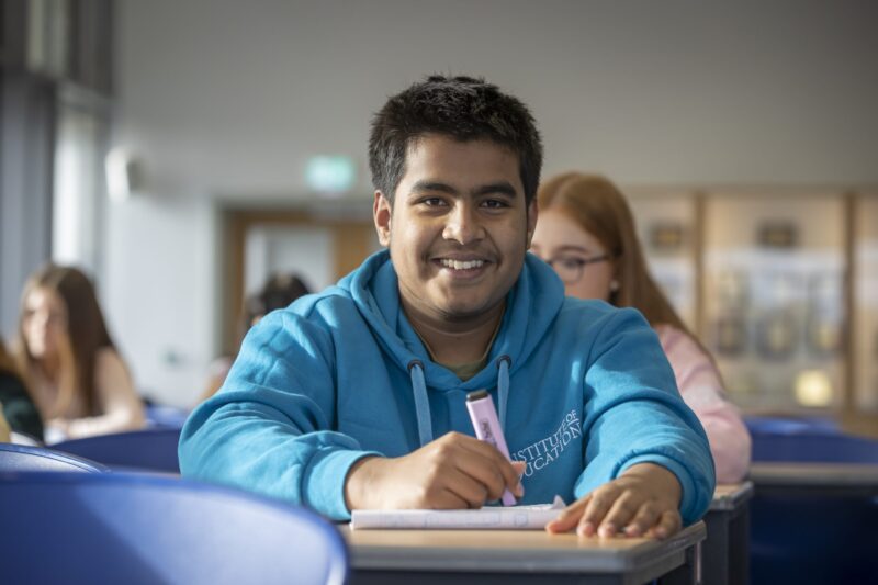a boy in a blue hoody sits at a desk and smiles