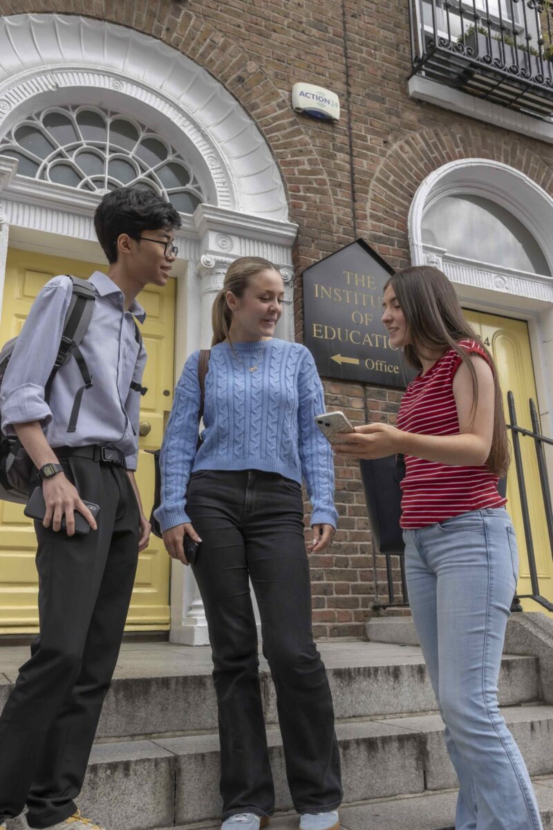 Three students chatting on the steps outside the Institute of Education's yellow front door.