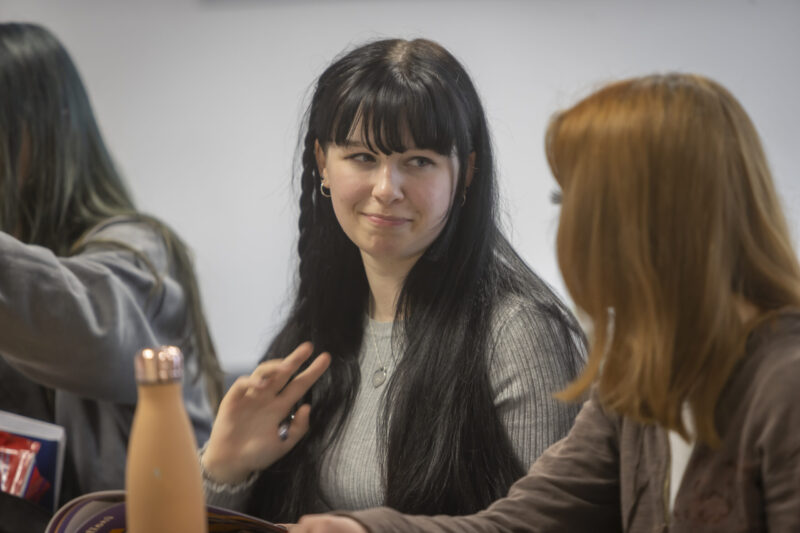 A student gesturing while talking with someone in a group setting.