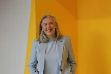 A photo of Jane D'Alton, standing in front of a yellow wall.
