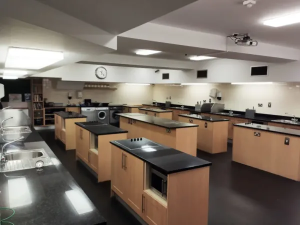 An empty home economics classroom with rows of kitchen workstations, each fitted with a hob and cabinets.