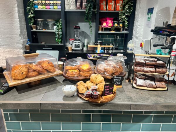 A café counter display of pastries, muffins and baked goods on a tiled worktop.
