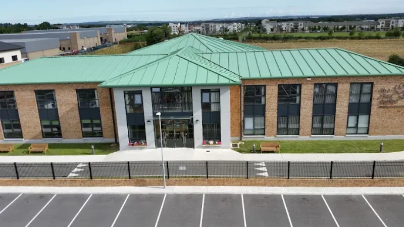 Aerial view of a modern two-storey brick building with a green metal roof, large windows, benches outside, a fenced perimeter, and a car park in the foreground—an ideal setting for leaving cert grinds in Swords.